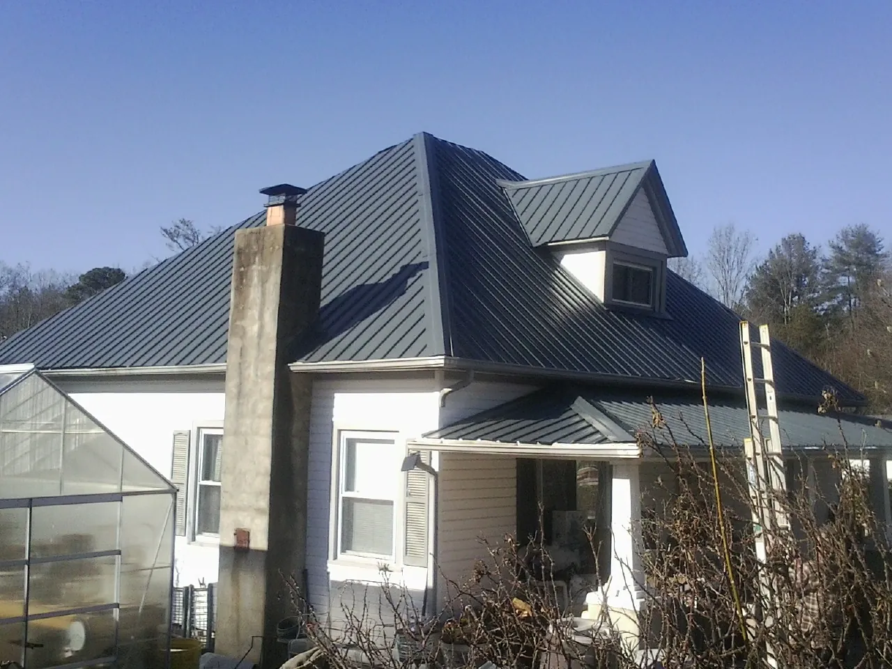 Dark blue standing seam metal roof on a white farmhouse with dormer — Slate & Tile Roof Repair by Roofing Brothers in Appomattox