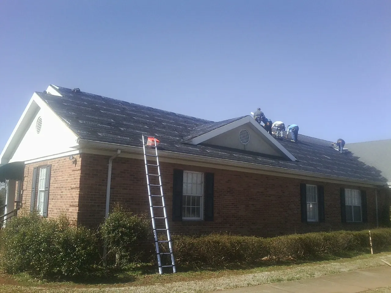 Crew tearing shingles off a brick ranch roof with a ladder set — Emergency Roof Repair work by our crew in Appomattox