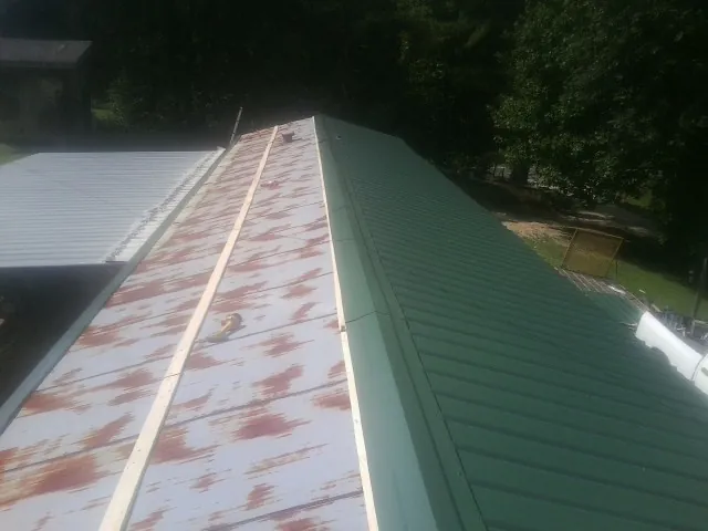 Old rusted panels beside newly installed green metal roofing — Wind Damage Roof Repair by Roofing Brothers in Appomattox