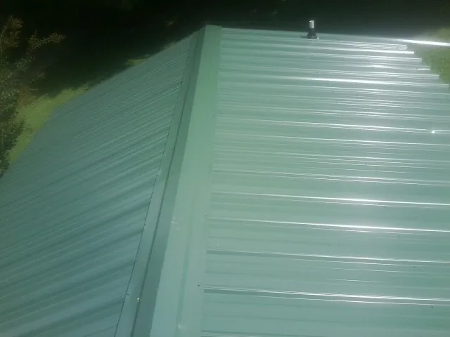 New green metal panels meeting at the ridge of a roof — Flat Roof Repair work by our crew in Appomattox