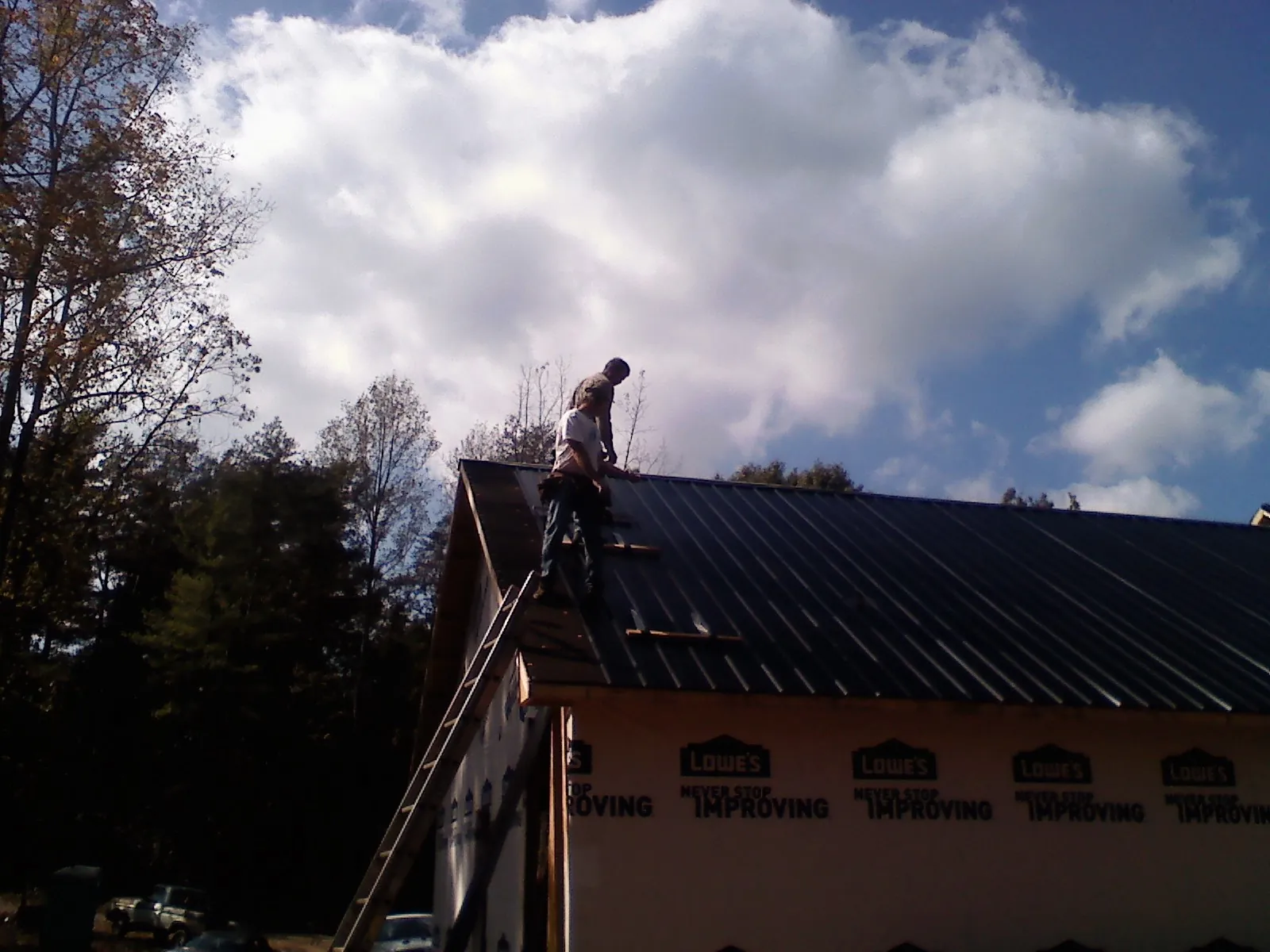 Roofer fastening dark metal panels high against a cloudy sky, from a Roof Inspection job in Appomattox