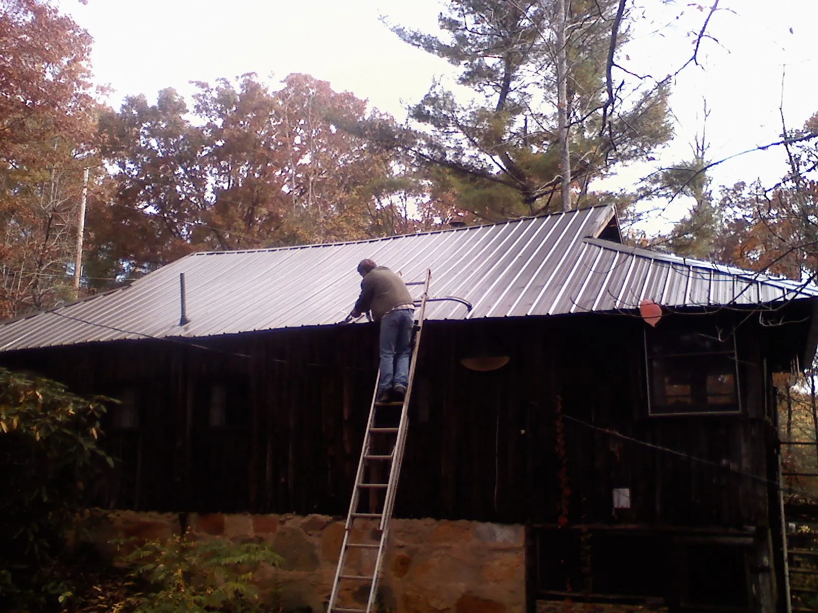 Roofer on a ladder working along the edge of a cabin metal roof in Appomattox