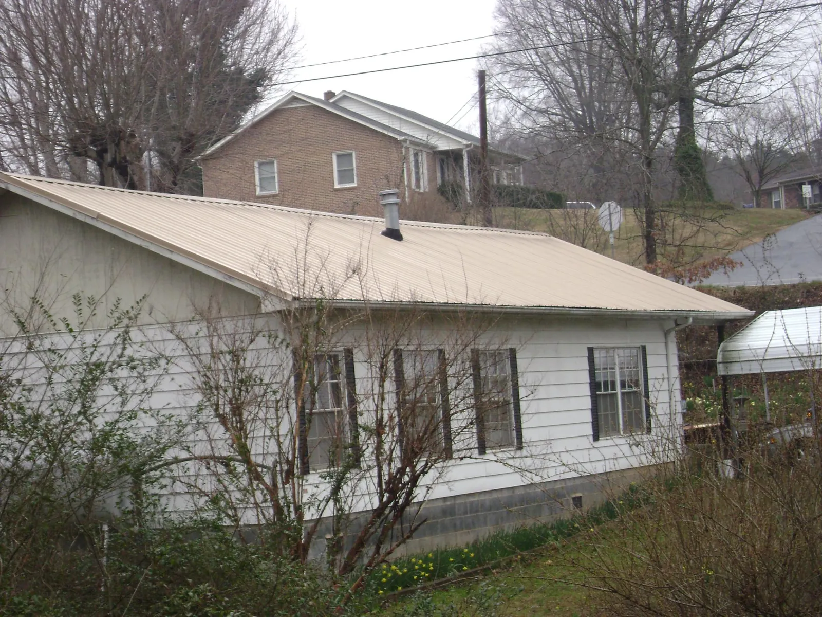 Tan metal roof on a white sided house set into a hillside — Commercial Roofing by Roofing Brothers in Appomattox